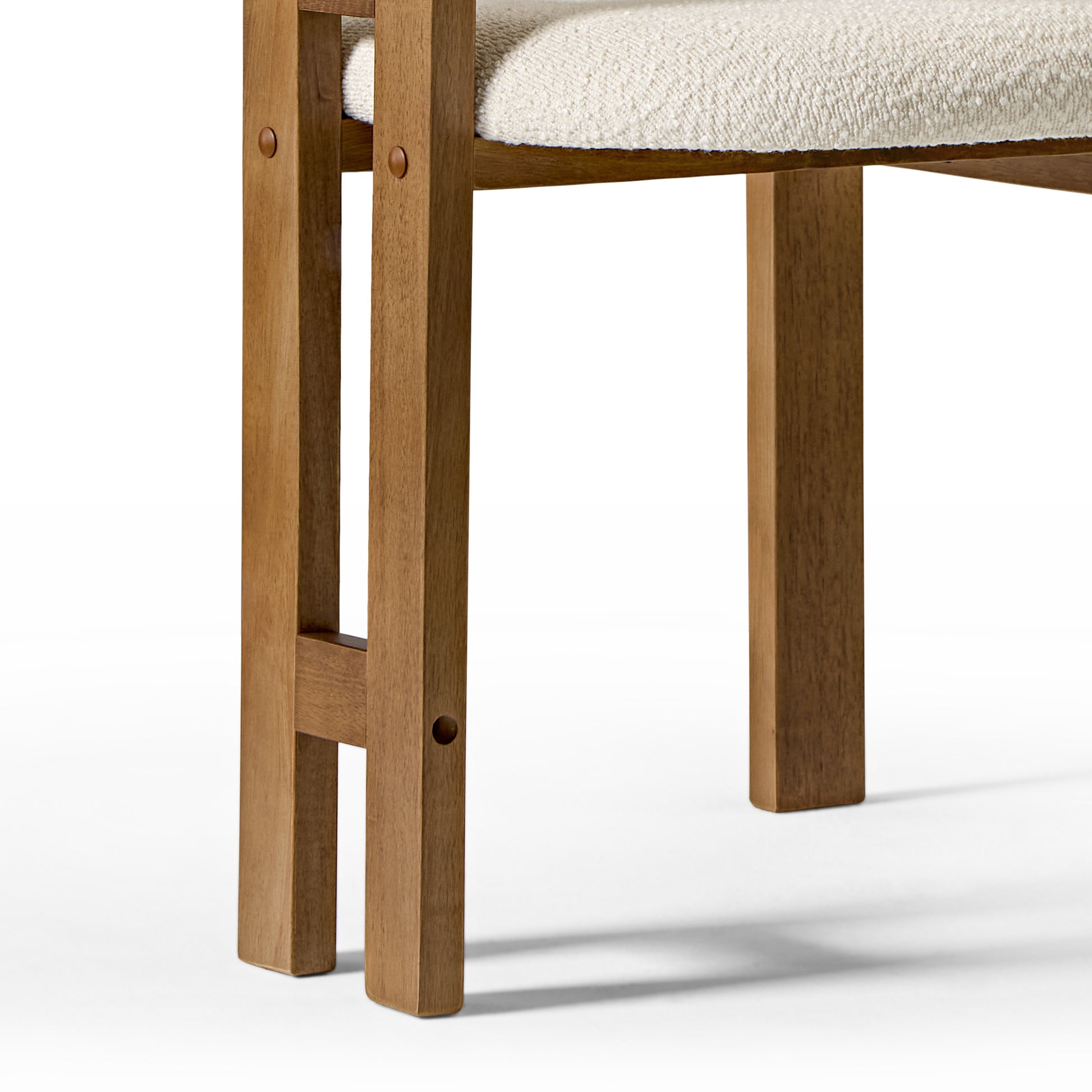 Eureka Ergonomic Close-up of ivory boucle dining chair seat edge and walnut wood frame showing dowel construction, mid-century modern detail.
