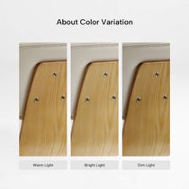 Eureka Ergonomic Off-white faux leather chair back showing stitching and light wood veneer under warm, bright, and dim light.