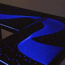 Eureka Ergonomic GTG L-shaped gaming desk with blue wave RGB lighting on tempered glass surface, starry night effect.