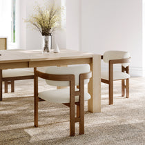 Eureka Ergonomic Two ivory boucle dining chairs with walnut frames and curved backs in a mid-century modern style, set in a dining room.