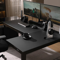 Eureka Ergonomic GTG L-shaped desk setup with dual monitors, keyboard, mouse, speakers, headphones, and cup on tempered glass surface.