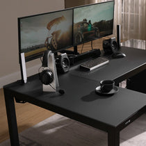 Eureka Ergonomic GTG L-shaped gaming desk with dual monitors, keyboard, mouse, speakers, and headphones setup on matte black glass.