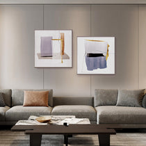 Set of 2 Abstract Wall Art Prints With Blue and Gold Geometric Designs Above Gray Sectional Sofa.