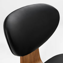 Eureka Ergonomic Close-up of black faux leather office chair backrest with curved walnut veneer shell and visible texture.