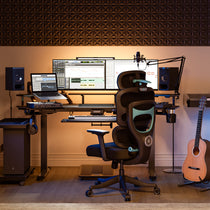 Eureka Ergonomic Axion ergonomic hybrid chair in black and teal, set up in a home studio with desk, monitors, and guitar.